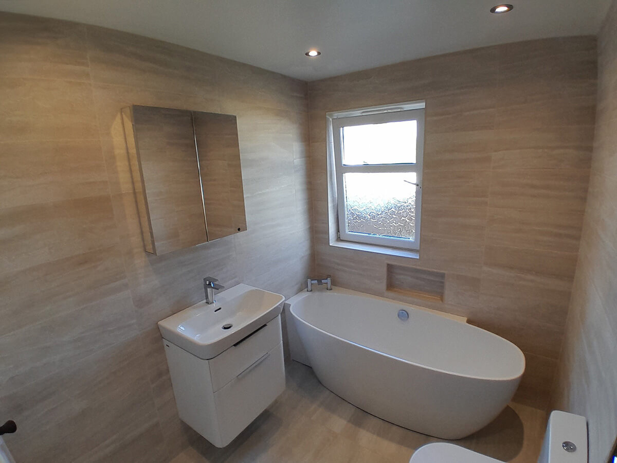 Completed bathroom renovation with freestanding oval bath, wall-mounted vanity unit and stone-effect tiled walls