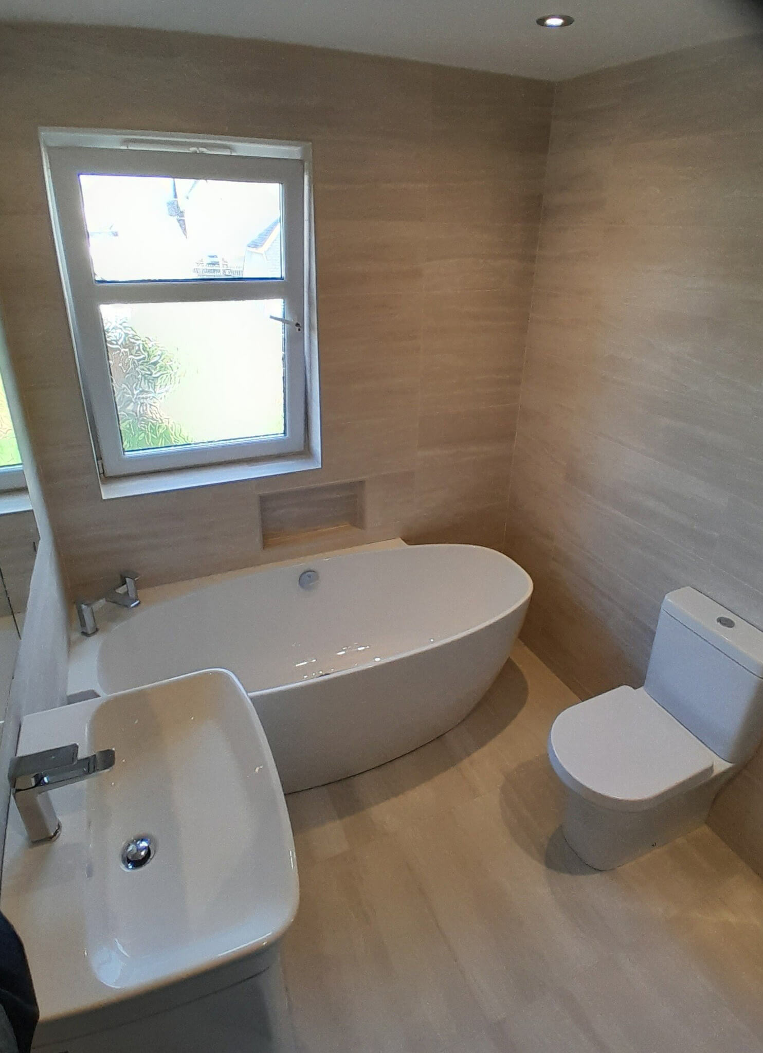 Renovated bathroom with freestanding oval bath, wall-mounted basin, WC and stone-effect tiling throughout