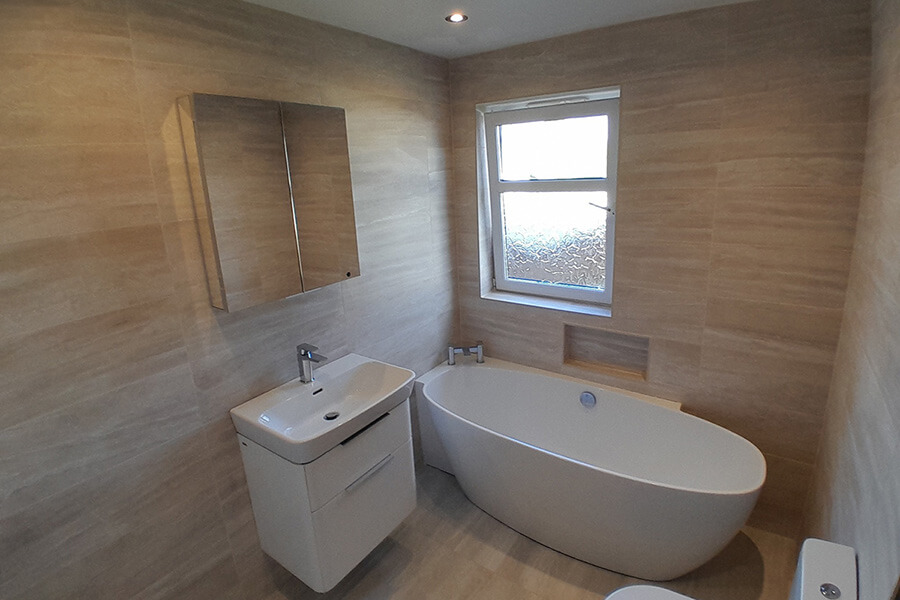 Modern bathroom transformation with freestanding oval bath, wall-hung vanity unit and full-height stone-effect tiles