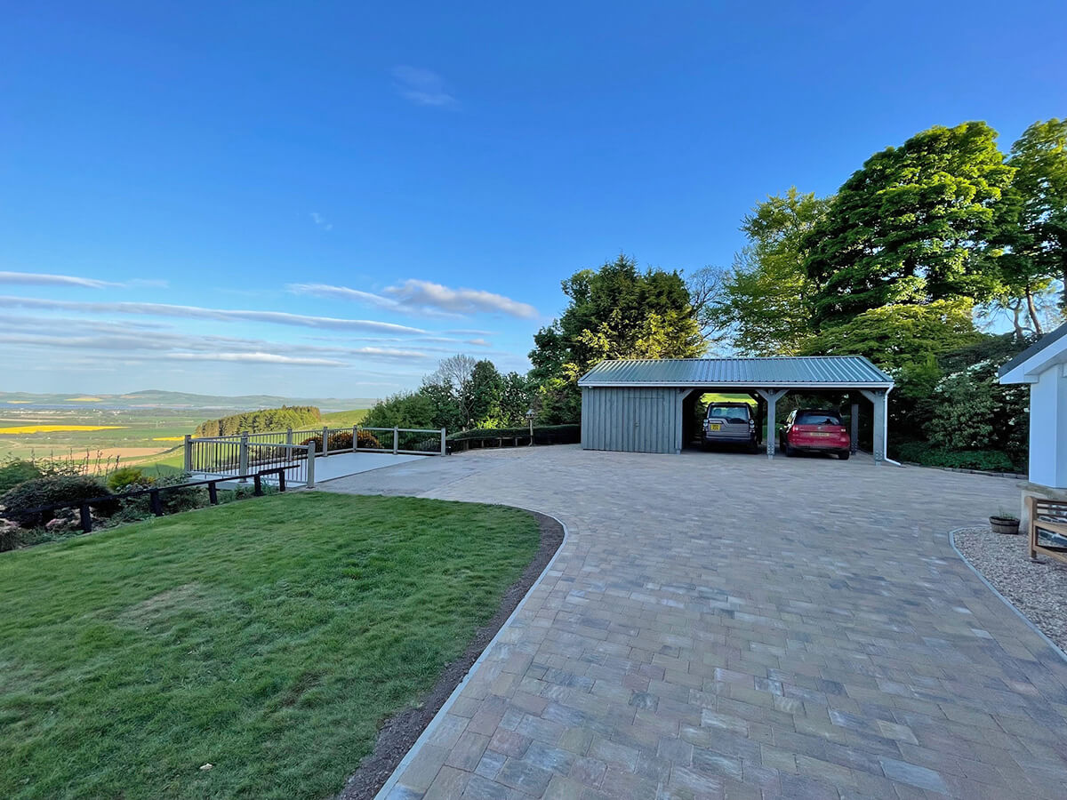 Wide view of completed car port and block-paved driveway with panoramic Perthshire countryside and cantilevered deck visible