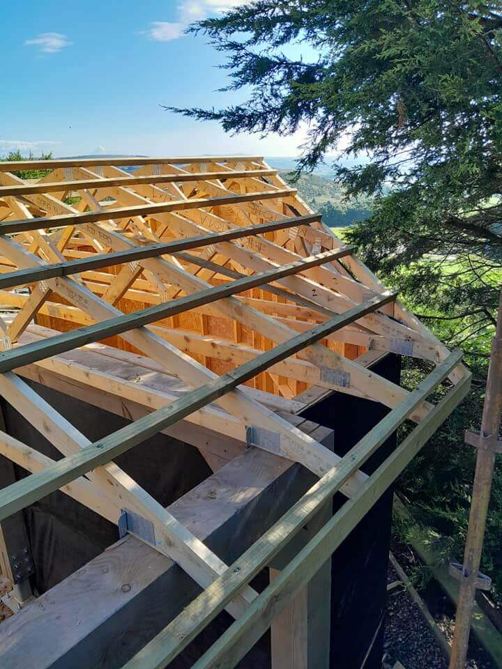 Close-up of roof trusses and rafters during car port construction, with countryside views beyond