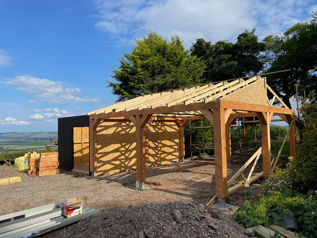 Timber car port frame with OSB panel walls and roof trusses visible, at mid-construction stage