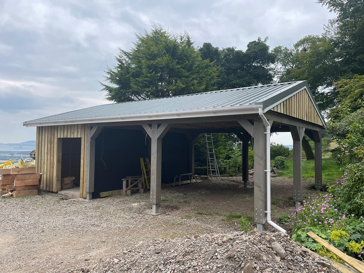 Car port structure with grey standing seam metal roof newly fitted, timber cladding and ladder on site
