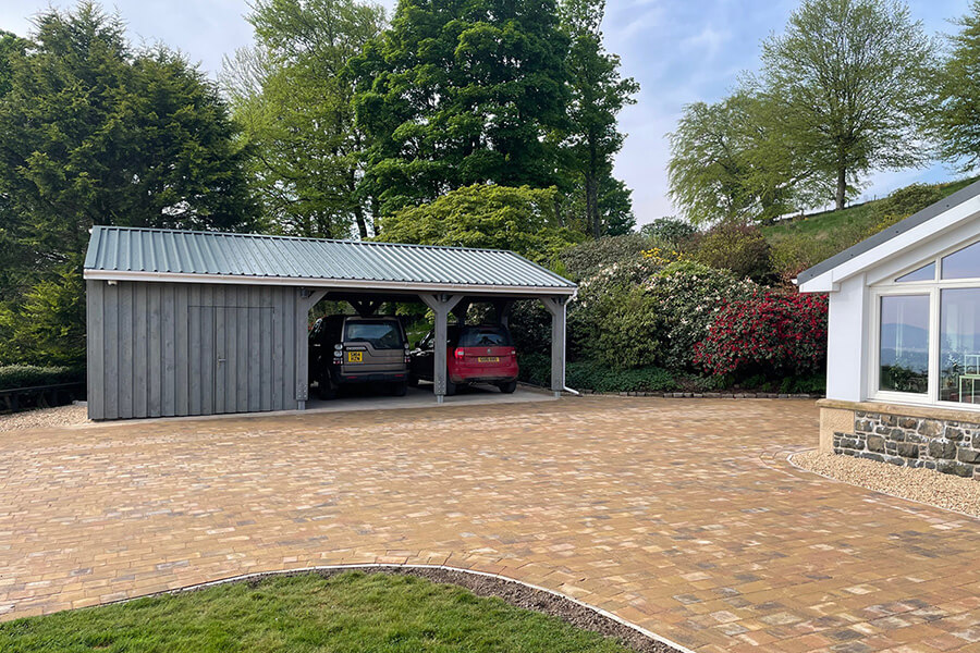 Timber-framed open car port with standing seam metal roof on a block-paved driveway