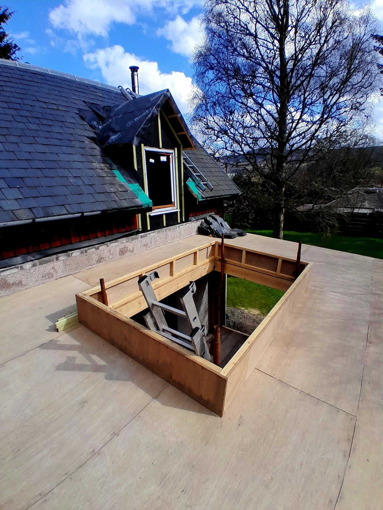 Bespoke rooflight upstand framed out on flat roof deck, scaffolding poles visible, Velux installation to main house roof in background