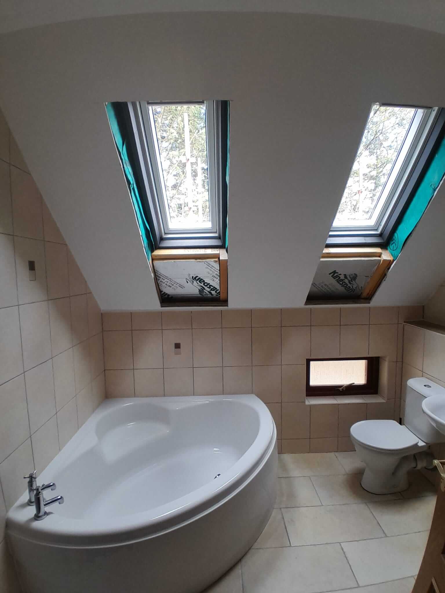 En-suite bathroom interior showing two new Velux rooflights freshly installed into vaulted ceiling above corner bath