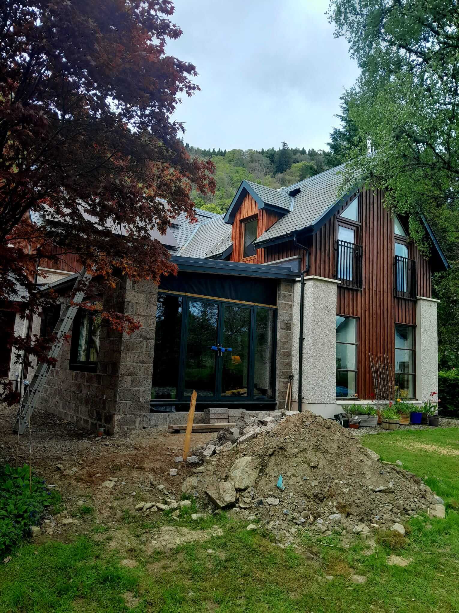 Near-complete extension from garden, anthracite aluminium bifold doors and glazing fitted, block base awaiting render, red Japanese maple in foreground