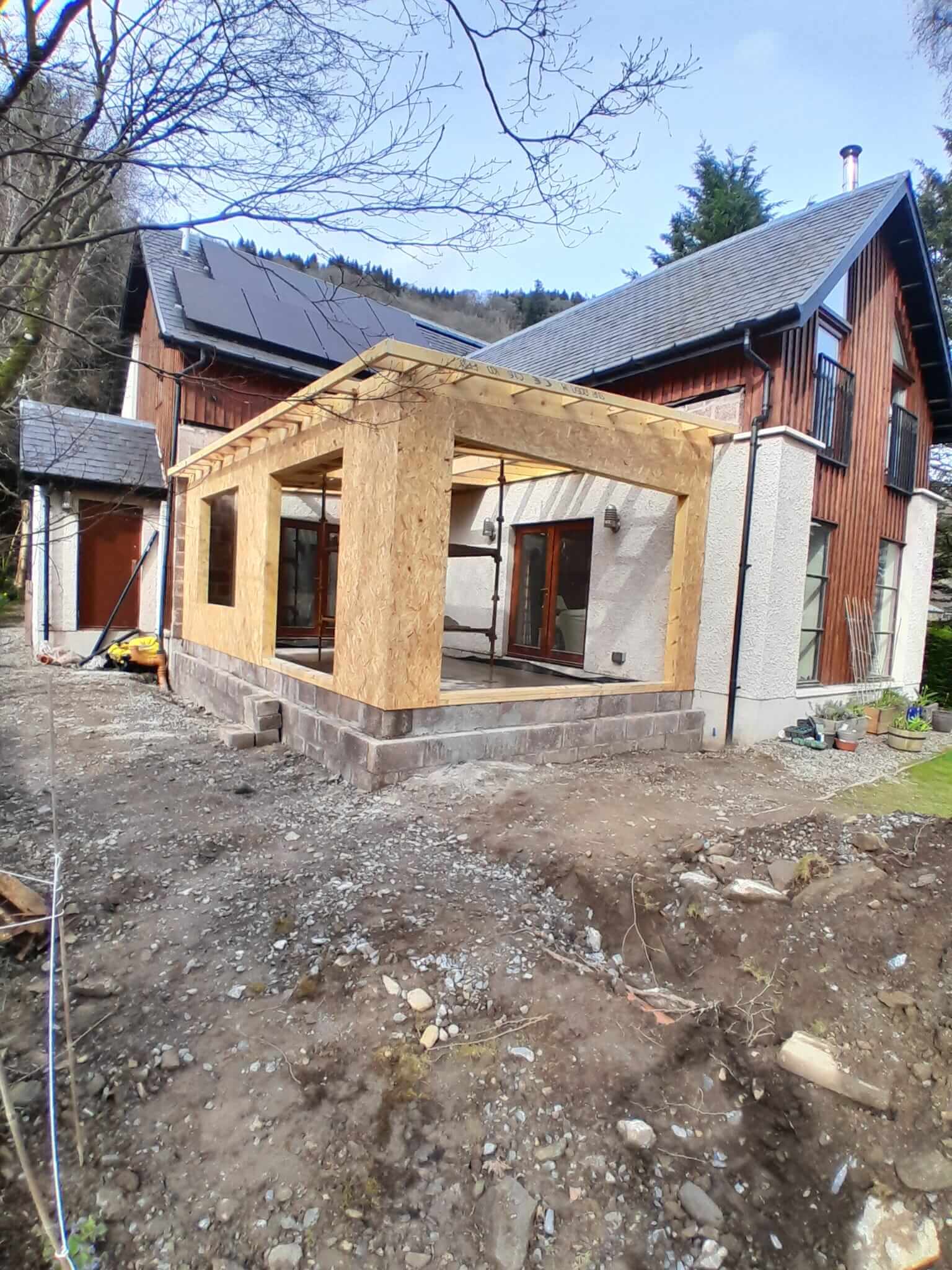 Full timber frame structure of single-storey extension with flat roof rafters, larch-clad original house behind