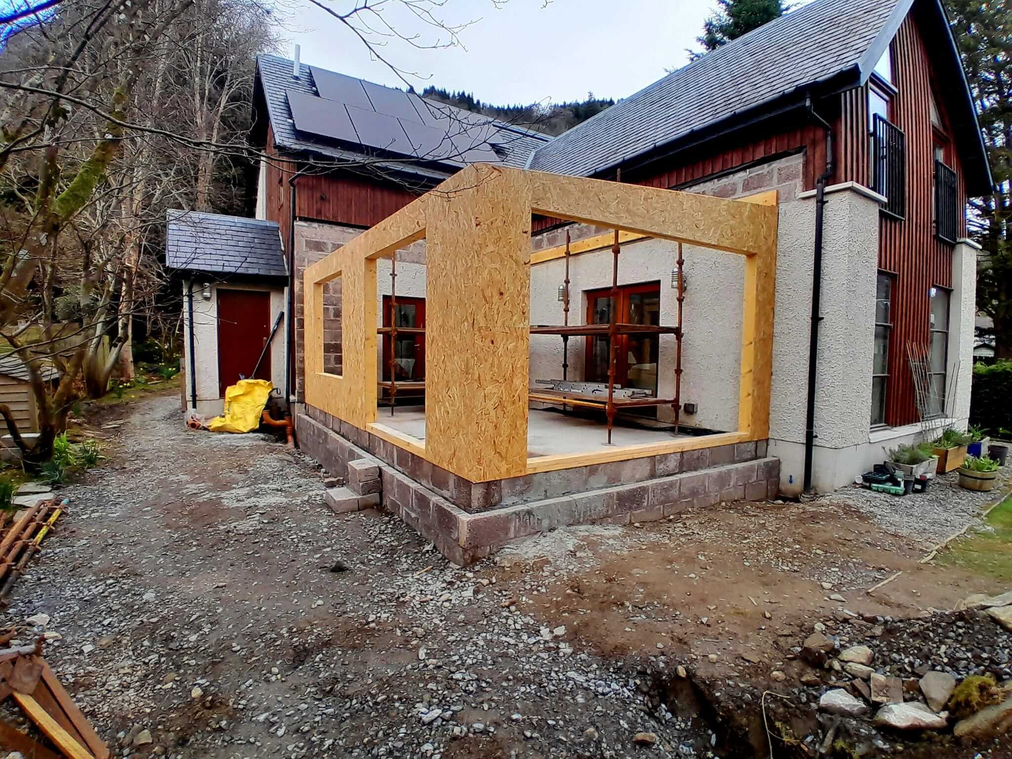 Front elevation of timber frame extension showing three large glazing openings before cladding, block base
