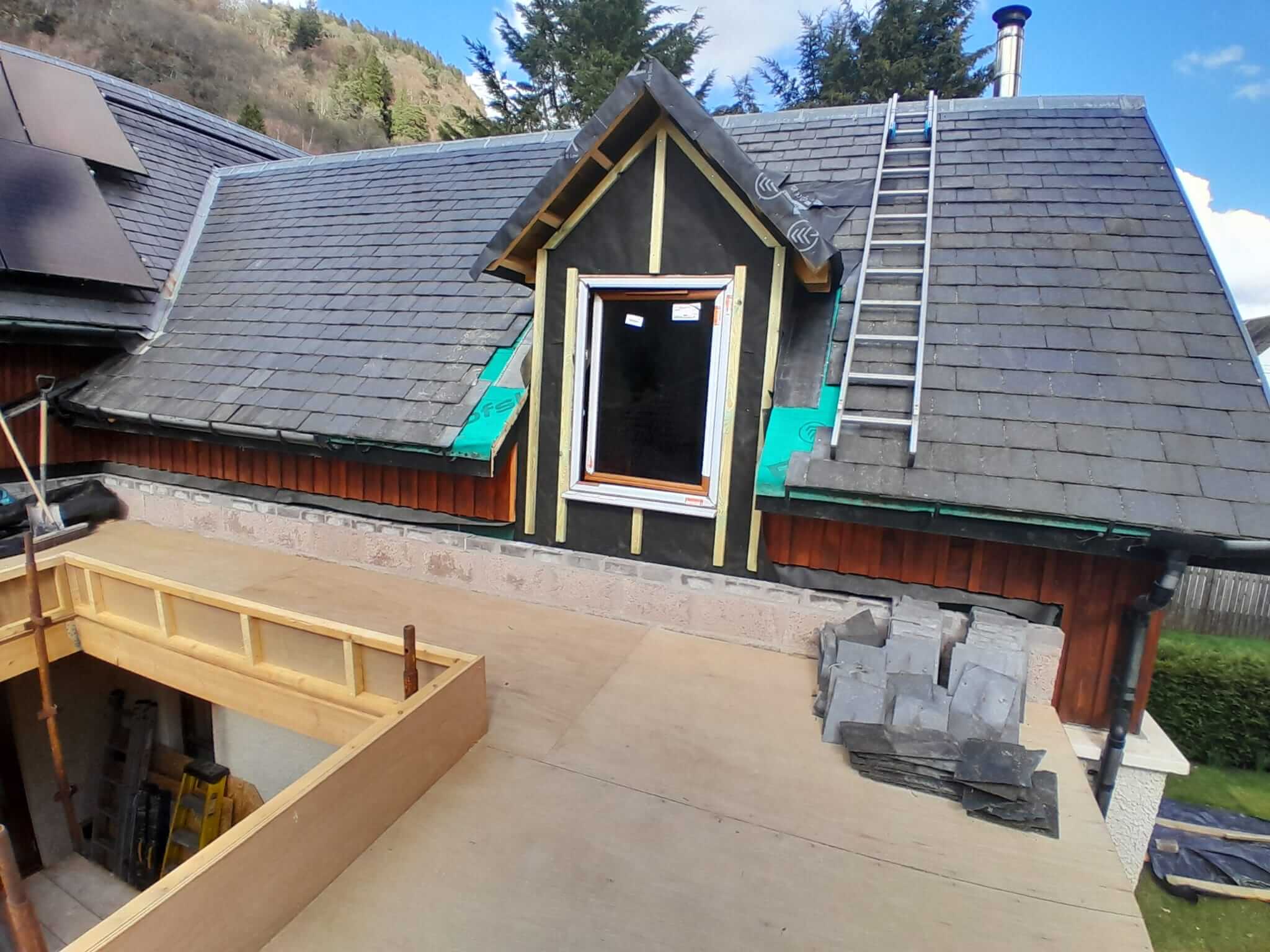 New Velux window installed in larch-clad dormer gable of existing house during slate re-laying works