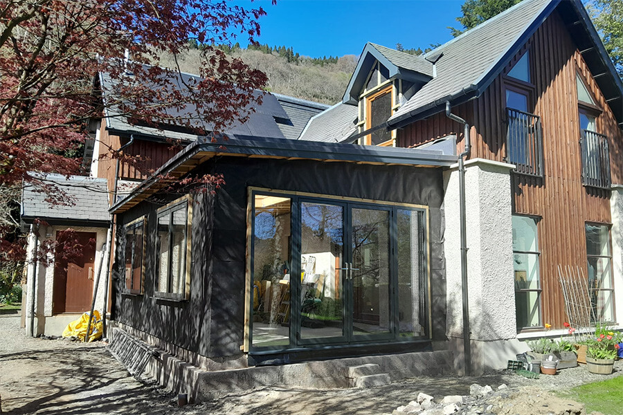 Single-storey residential extension at Weem, featuring anthracite aluminium bifold doors and large glazed windows, flat roof with dark cladding complementing the existing larch-clad two-storey house