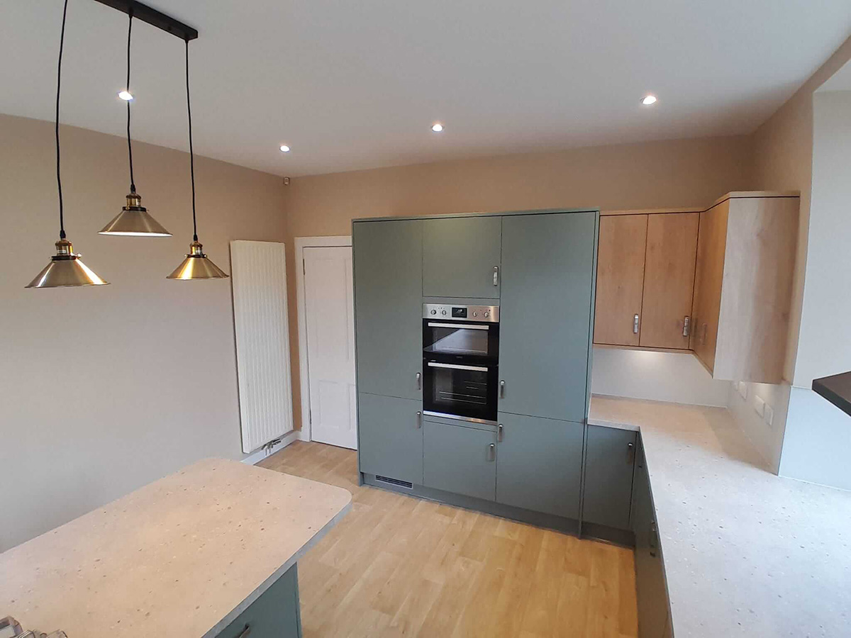 New sage green kitchen units being installed with quartz island worktop during renovation