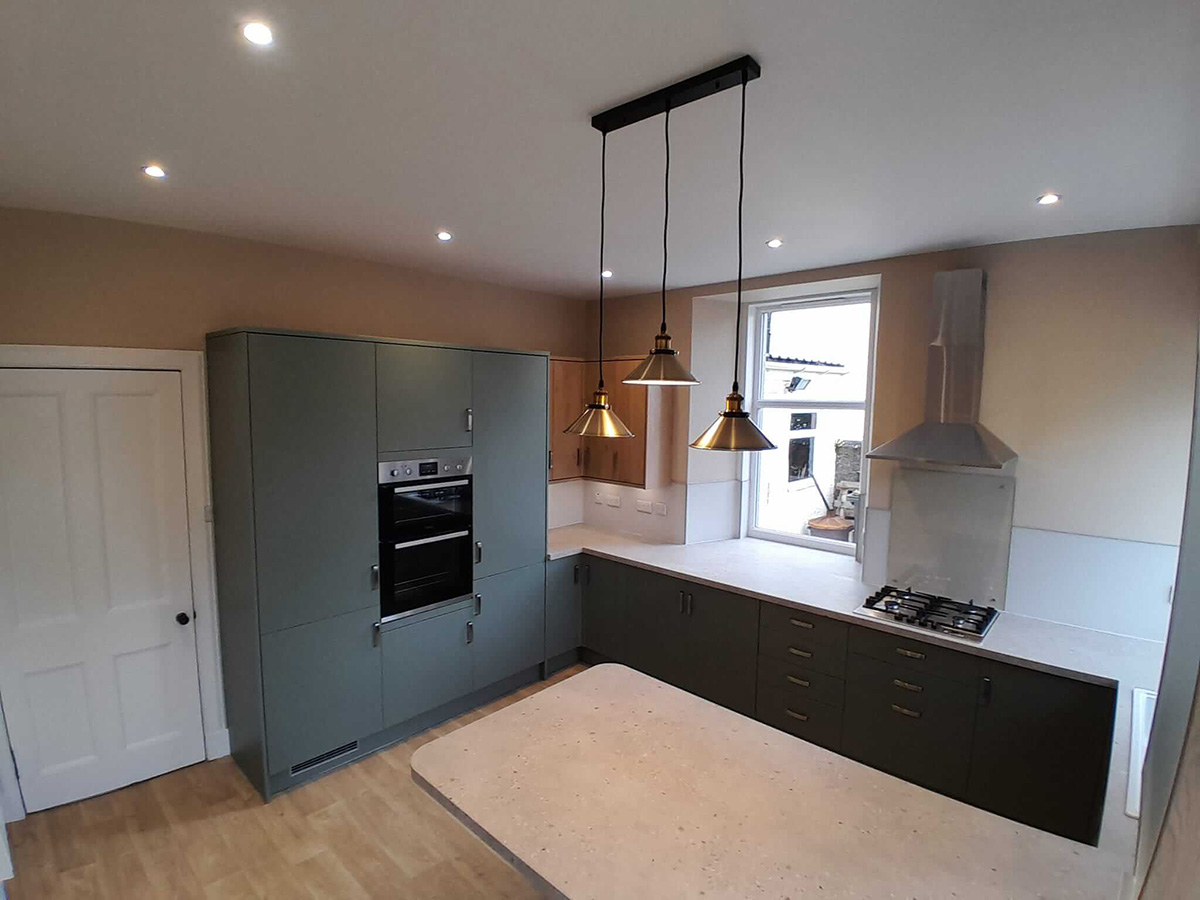 Completed kitchen renovation with sage green flat-front cabinets, quartz worktops, brass pendant lights and oak flooring