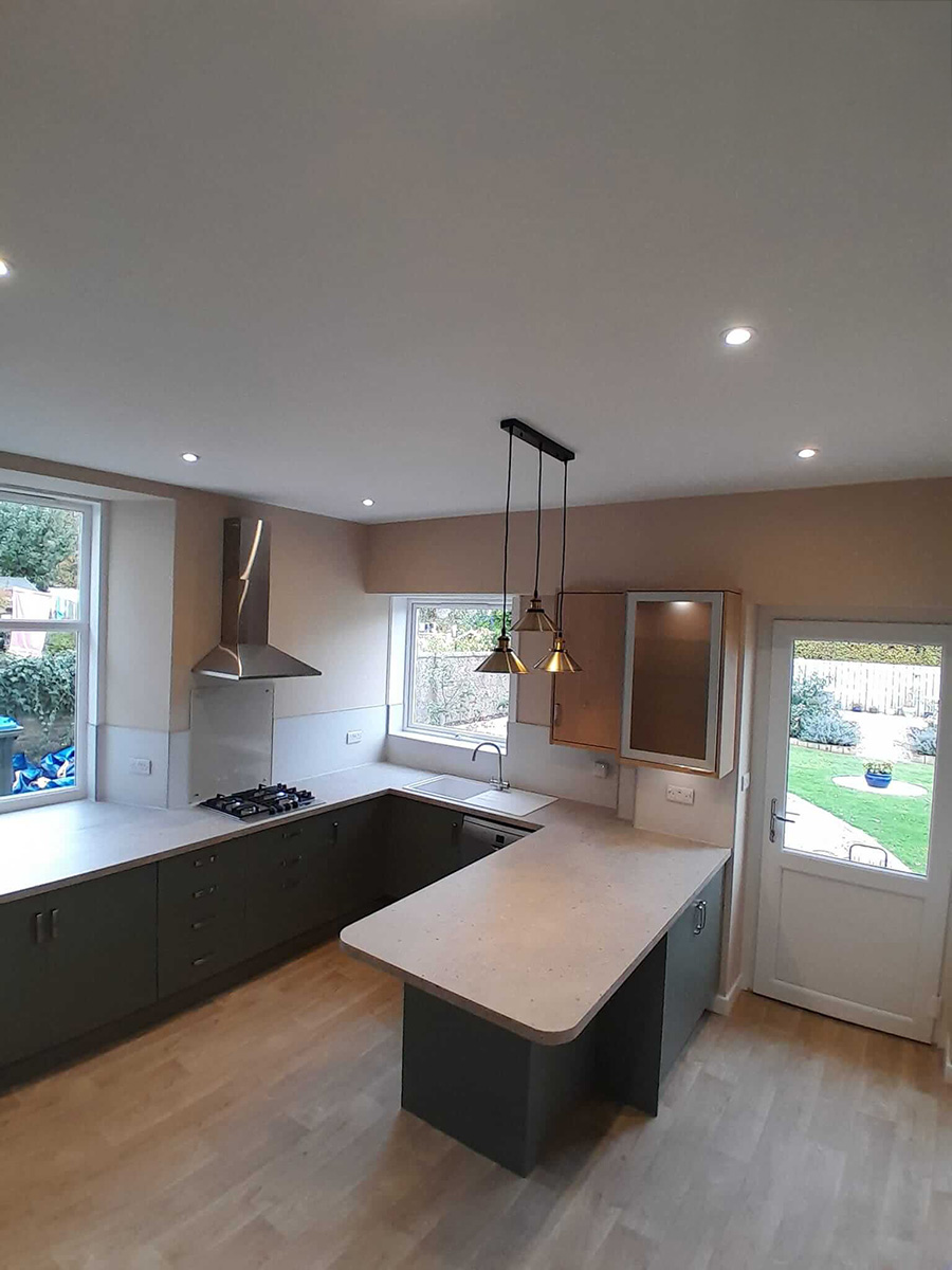 Renovated kitchen showing the central island, brass pendant lights, gas hob, wall extractor and garden views