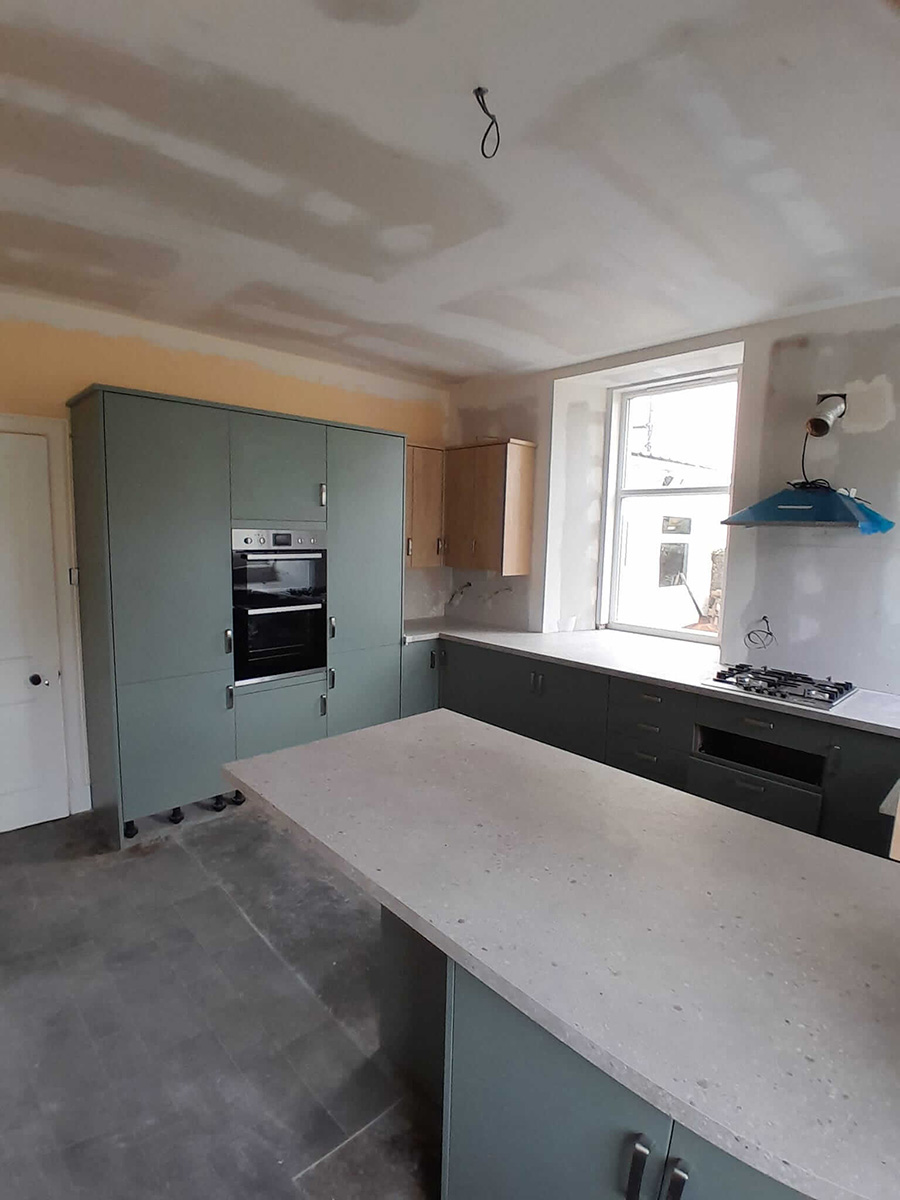 Wide-angle view of completed kitchen renovation with central island, pendant lights and French doors to the garden