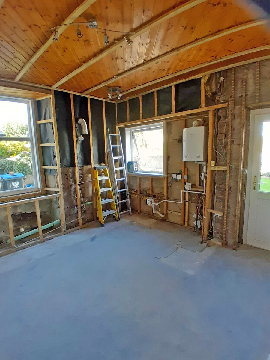 Kitchen stripped back to bare timber frame structure with exposed plumbing and concrete screed floor