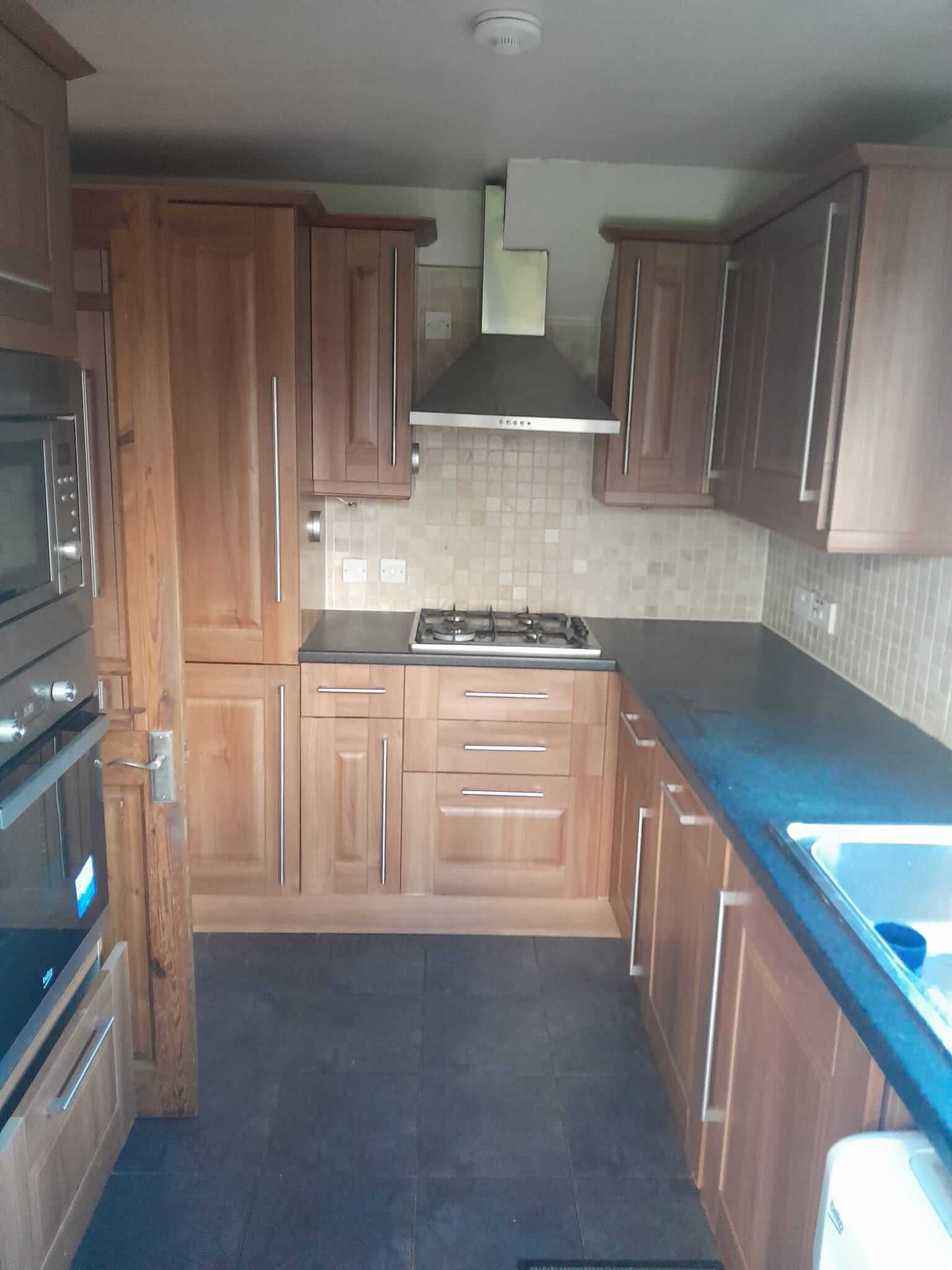 Original kitchen before works with dark walnut cabinets, dark granite worktops and mosaic splashback