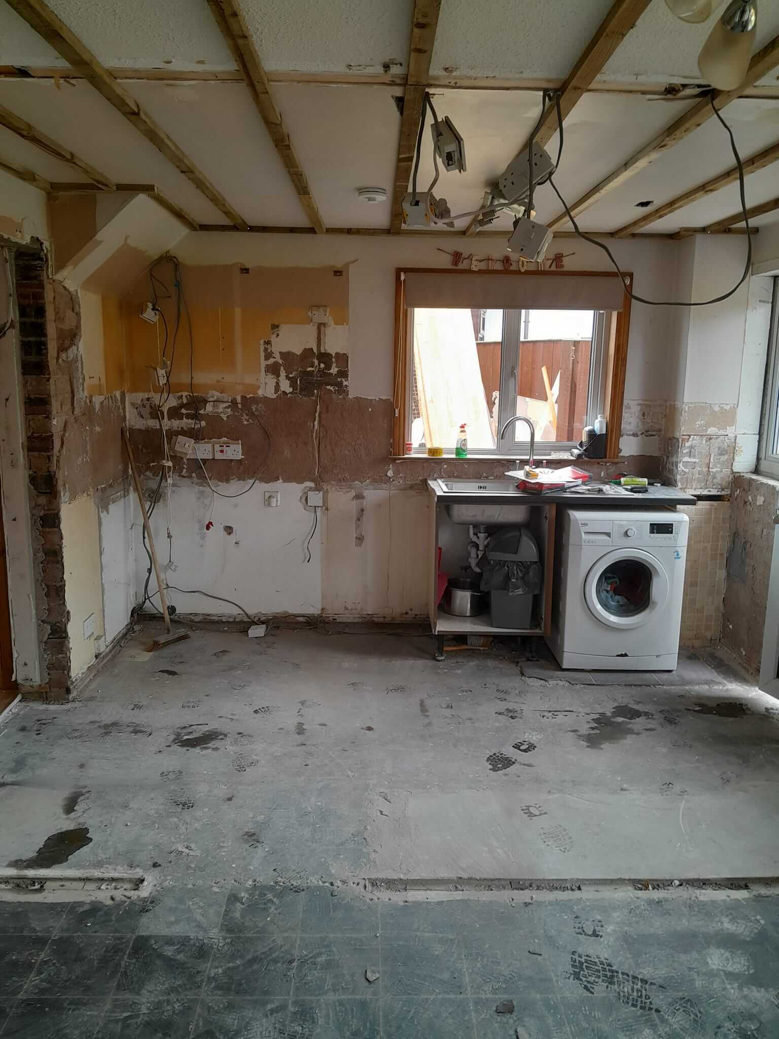 Kitchen fully stripped out with bare concrete floor and exposed ceiling timbers, ready for rebuild