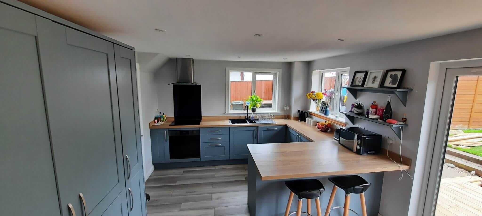 Completed open-plan kitchen and dining area with blue-grey shaker cabinets, oak worktops, peninsula and bar stools