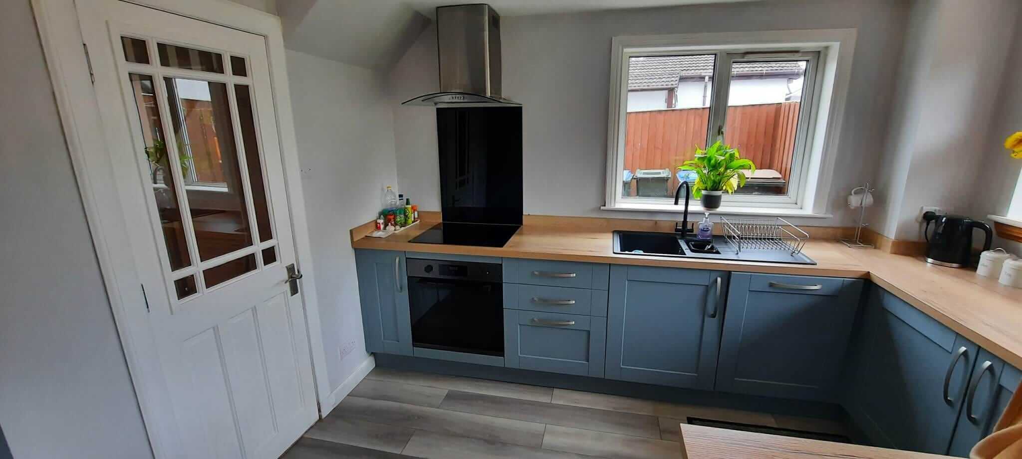 Completed open-plan kitchen with blue-grey shaker cabinets, oak worktops, black induction hob and stainless steel extractor