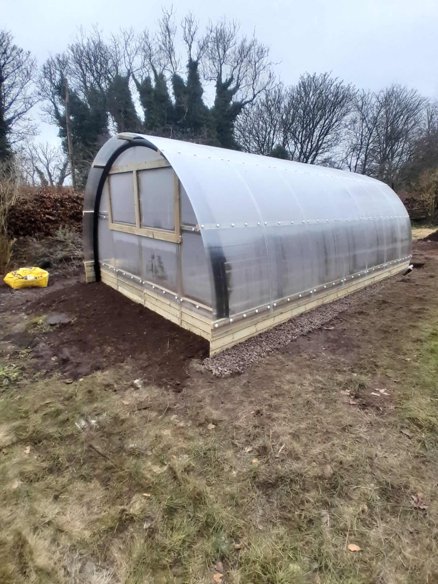 Three-quarter exterior view of Poly Crub tunnel showing custom fabricated stable door and window in gable end, gravel path alongside